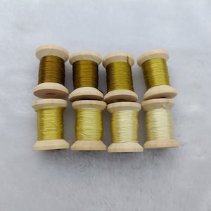 May include: Eight spools of thread, four are a light yellow color and four are a darker yellow-green color. The spools are made of wood and have a natural finish.