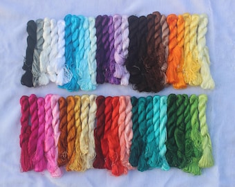 May include: A collection of embroidery floss skeins arranged in two horizontal rows, featuring a wide spectrum of colors including black, white, gray, various shades of blue, purple, brown, orange, yellow, pink, red, and multiple tones of green.