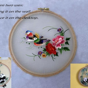 Puede incluir: Obra de arte bordada en un aro de madera con dos patos mandarines coloridos, flores rosas y rojas, y el texto "There are two uses: 1. Hang it on the wall. 2. Place it on the desktop."