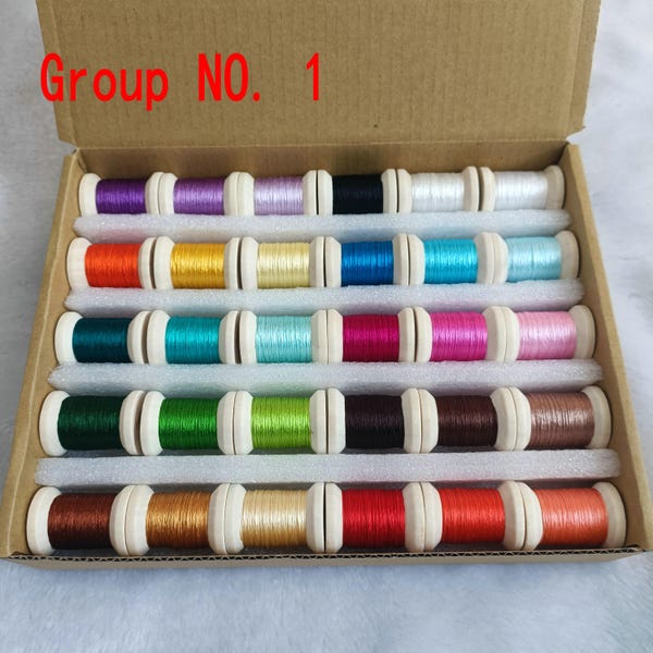 Op de afbeelding: Een kartonnen doos met het label Group NO. 1 bevat dertig houten klossen borduurgaren in verschillende kleuren, waaronder paars, blauw, groen, rood, geel en bruin, gerangschikt in vijf rijen gescheiden door witte schuimrubberen verdelers.