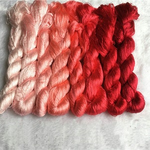 May include: Five spools of embroidery floss in a gradient of pink, red, and orange colors.