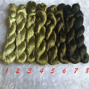 Puede incluir: Ocho carretes de hilo de bordar verde, numerados del 1 al 8, dispuestos en un degradado de verde claro a verde oscuro.