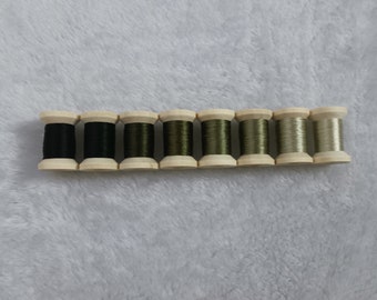 Könnte beinhalten: Zehn Spulen mit Garn in verschiedenen Grüntönen und Beige. Die Spulen sind aus Holz und haben eine natürliche Oberfläche.