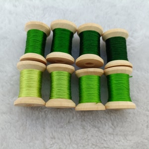 May include: Eight spools of green and lime green thread wound on wooden spools.