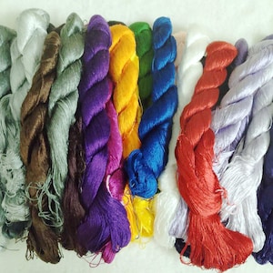 May include: Assortment of 12 spools of embroidery floss in various colours, including grey, brown, purple, yellow, green, blue, red, and white.