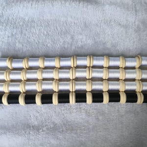 May include: Four rows of thread spools with light-colored wooden ends. Three rows feature white thread, labeled #88-3, #88-2, and #88-1. The bottom row features black thread, labeled 88-4. Each spool is aligned horizontally in a grid-like arrangement.