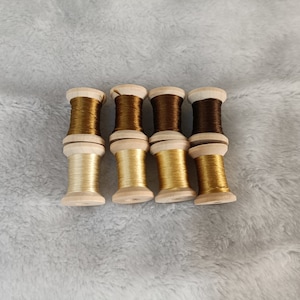 May include: Six spools of thread in various shades of brown and gold, wound on wooden bobbins.