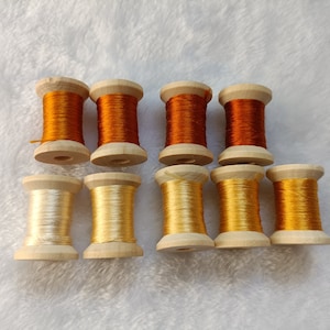 Puede incluir: Diez carretes de hilo, la mitad son de color naranja y la mitad son de color crema, en carretes de madera.