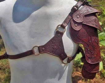 May include: Brown leather shoulder armor with decorative embossed details. The armor is worn on a white mannequin.