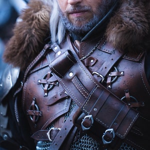 May include: A man dressed as Geralt of Rivia from the Witcher video game series. He is wearing a brown leather armor with a fur collar, a white wig, and has yellow contact lenses.