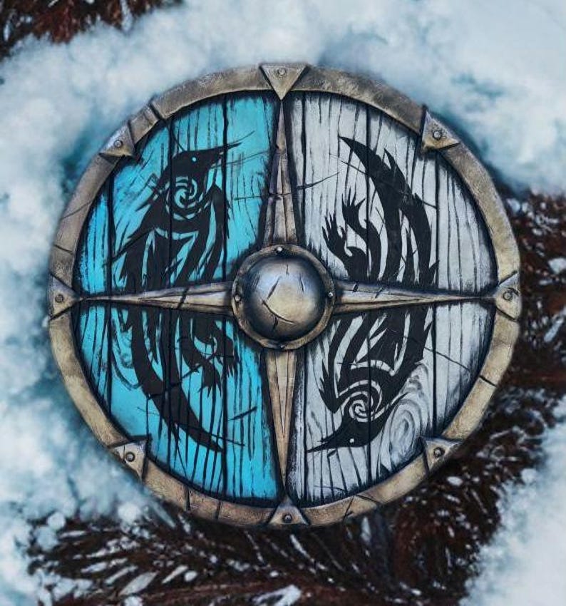 May include: A round wooden shield with a metal rim. The shield is painted in half blue and half white. Each half features a black stylized bird design.