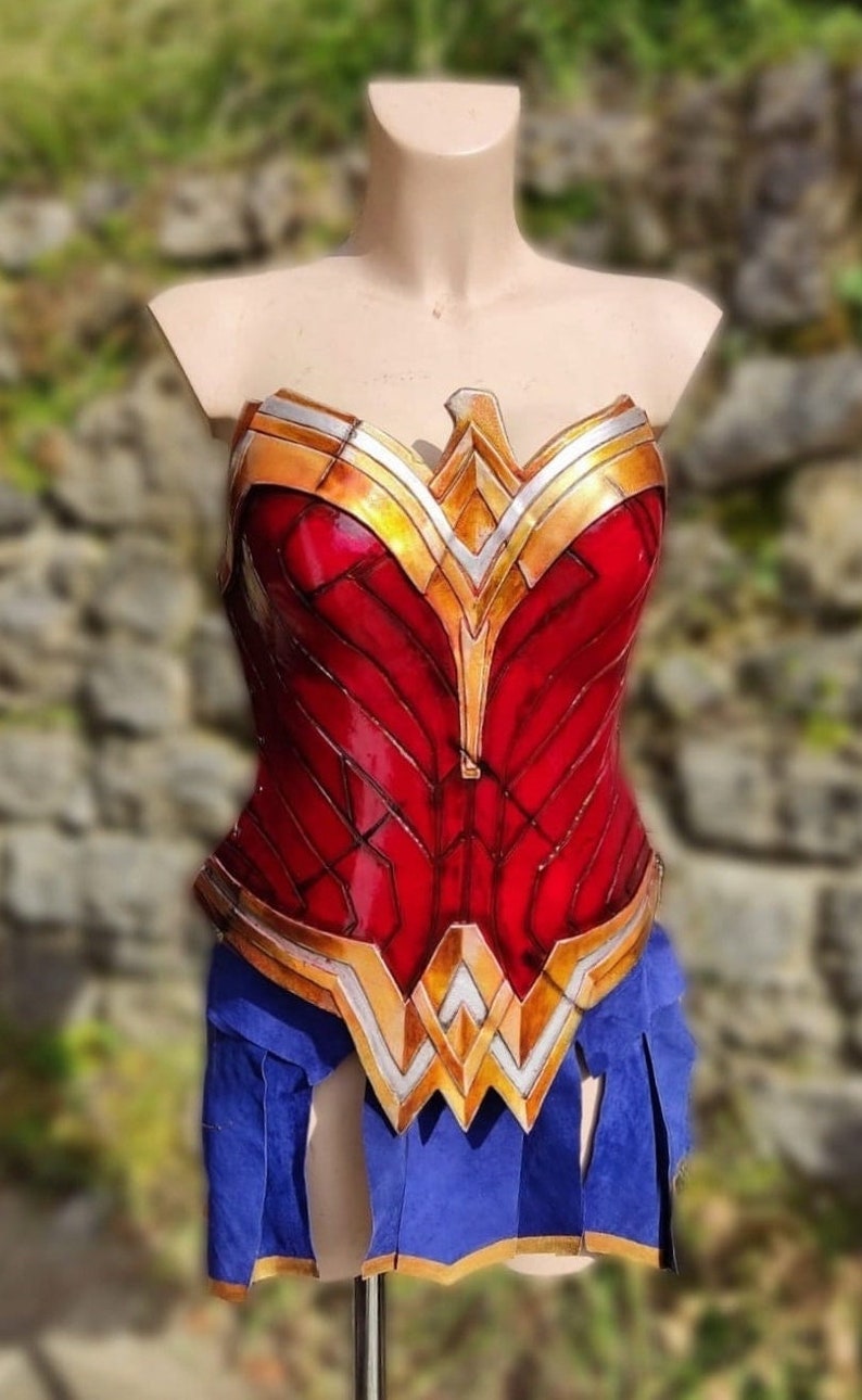 Op de afbeelding: Een rood en gouden Wonder Woman kostuum-bovenstuk met een gedetailleerd ontwerp. Het bovenstuk is gemaakt van een glanzend materiaal en heeft een gesculpteerde look.