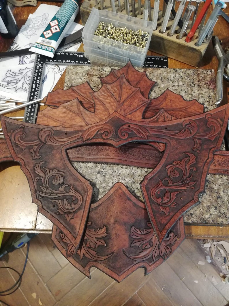 May include: Close-up of a leather craft project, featuring multiple pieces of brown leather with intricate floral designs carved into the surface. The leather pieces are arranged on a wooden surface.