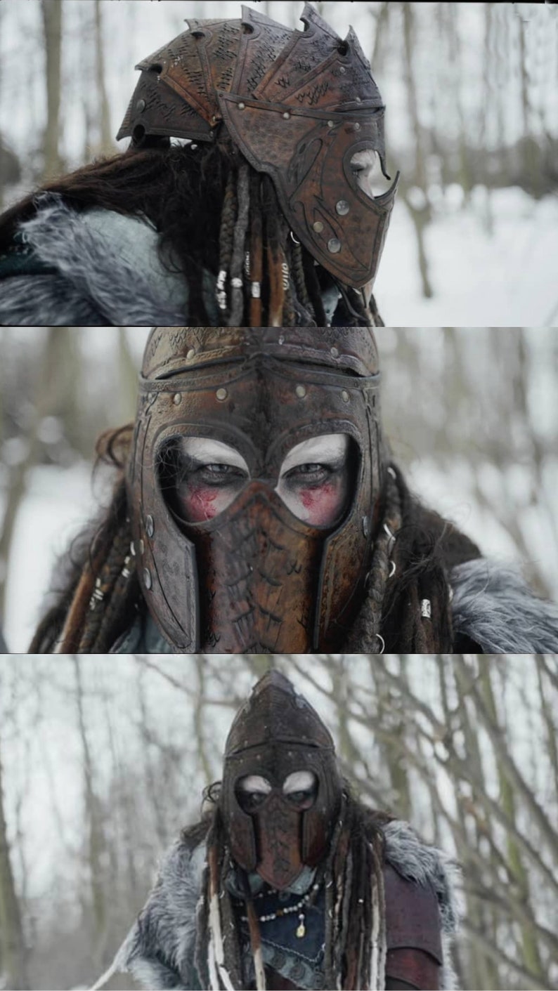 May include: A person wearing a brown leather helmet with intricate carvings and a face mask. The helmet has a pointed top and is decorated with metal studs. The person has long, dark hair and is wearing a fur-lined coat.