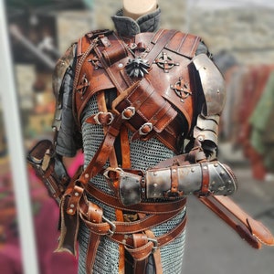 May include: A brown leather and metal costume with a chainmail shirt, multiple straps, and a silver pendant. The costume is displayed on a mannequin.