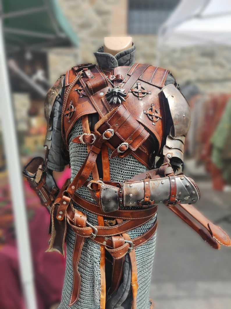 May include: A brown leather and metal costume with a chainmail shirt, multiple straps, and a silver pendant. The costume is displayed on a mannequin.