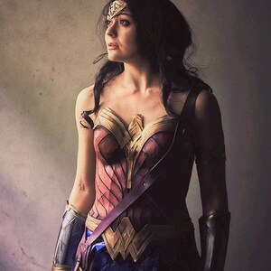Op de afbeelding: Een vrouw verkleed als Wonder Woman, draagt een rood, goud en bruin kostuum met een gouden tiara en armbanden. Ze kijkt omhoog en naar rechts.
