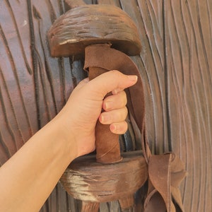 May include: A brown wooden shield with a leather strap and handle. The handle is wrapped in brown leather and has a textured surface.