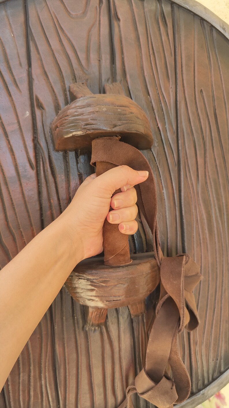 May include: A brown wooden shield with a leather strap and handle. The handle is wrapped in brown leather and has a textured surface.