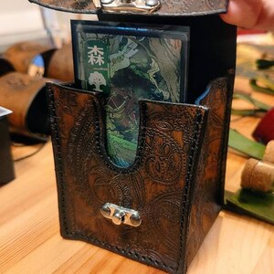 May include: A brown leather card deck box with a paisley pattern and a metal clasp. The box is open and a card with Japanese text is visible inside.