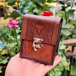 May include: A brown leather card case with a silver clasp and a textured surface. The case has a symbol embossed on the front.