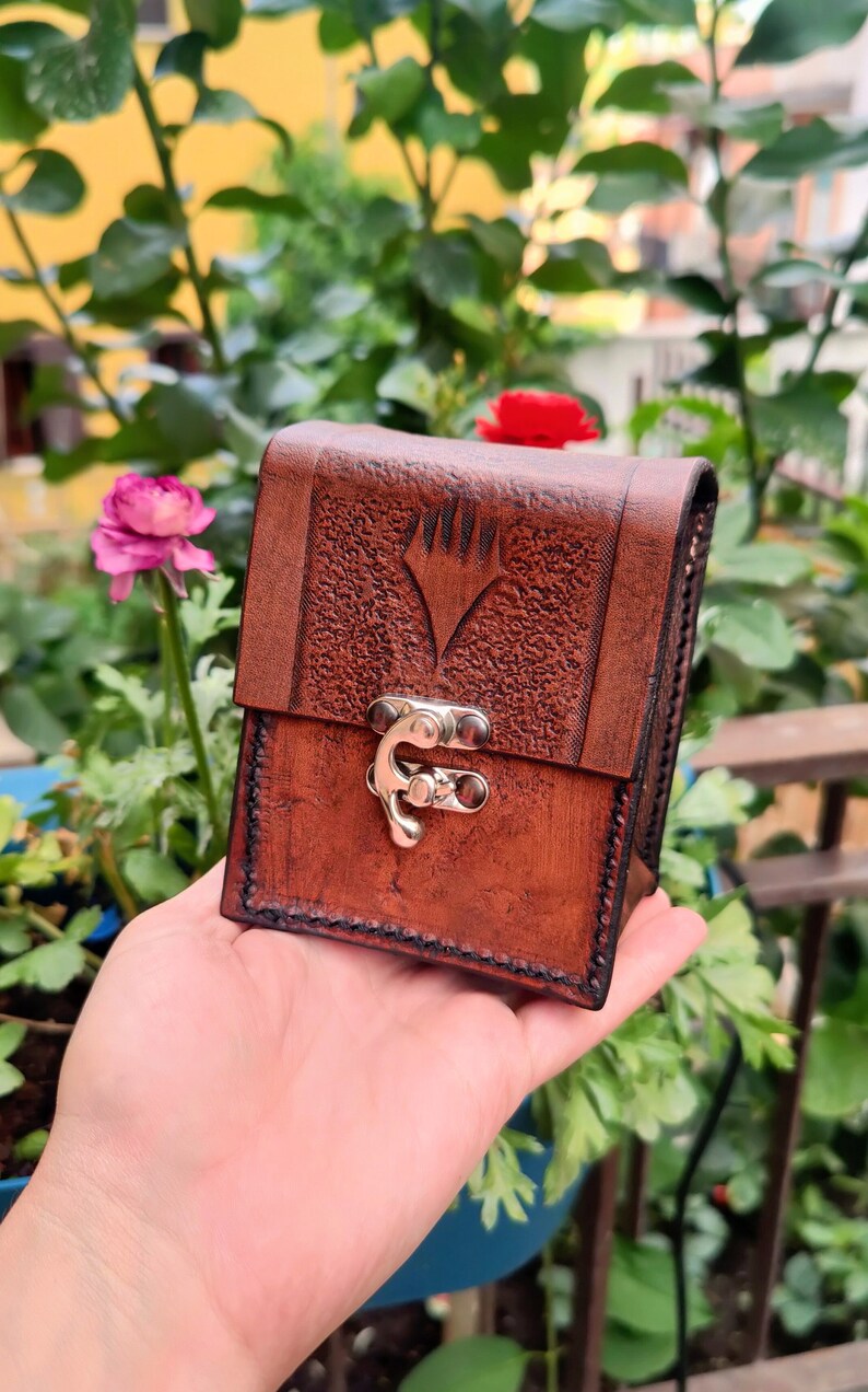 May include: A brown leather card case with a silver clasp and a textured surface. The case has a symbol embossed on the front.