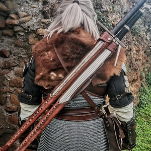 May include: A brown leather scabbard with two silver swords strapped to the back of a person wearing a brown fur-lined jacket and chainmail.