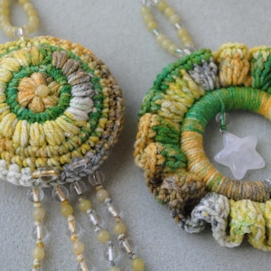 May include: Two crocheted ornaments with a star-shaped charm. One ornament is a circle with a green, yellow, and white pattern. The other ornament is a ring with a green, yellow, and white pattern.