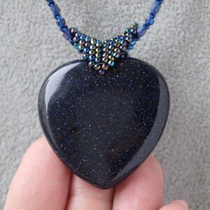 May include: A dark blue heart-shaped pendant made of blue sand stone with a beaded cord necklace.