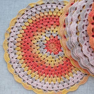 Puede incluir: Un conjunto de tapetes de ganchillo hechos a mano en tonos naranja, amarillo y gris. Los tapetes circulares tienen un borde festoneado y un dise&ntilde;o calado detallado. Los colores del hilo crean un efecto degradado.
