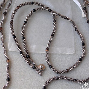 Op de afbeelding: Een zilveren en zwarte kralenketting met een magneetsluiting. De ketting is gemaakt met kleine, ronde kralen en heeft verschillende kleuren, waaronder zilver, zwart en bruin.