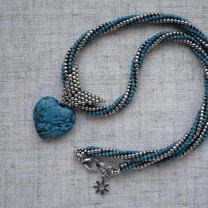 May include: A blue and silver beaded necklace with a turquoise heart pendant.
