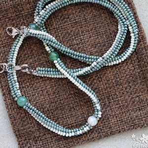 May include: A multi-strand necklace with green and white beads and green gemstone accents. The necklace is made of small beads and has a silver clasp.