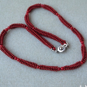 May include: A red beaded necklace with a silver clasp. The necklace is made of small, round beads and has a multi-strand design. The beads are a deep, rich red color.
