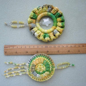 May include: Two crocheted dreamcatchers with beads. The top dreamcatcher is yellow, green and white with a star-shaped charm. The bottom dreamcatcher is green, yellow and white with a beaded fringe.