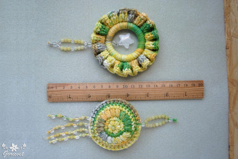 May include: Two crocheted dreamcatchers with beads. The top dreamcatcher is yellow, green and white with a star-shaped charm. The bottom dreamcatcher is green, yellow and white with a beaded fringe.