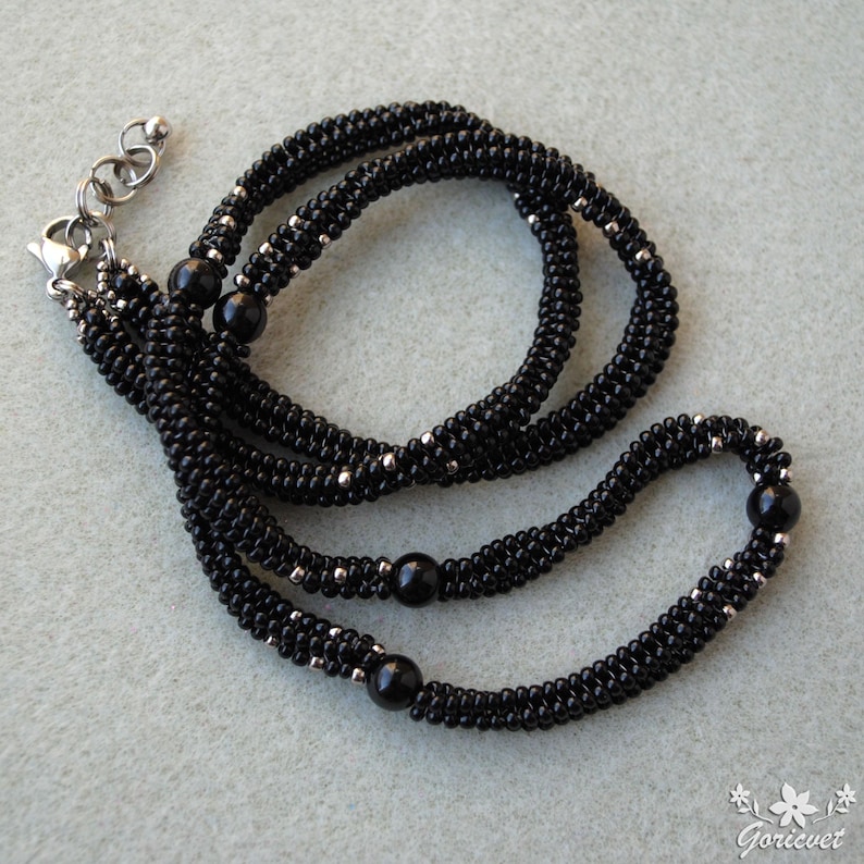 May include: A black beaded necklace with three strands. The necklace features small, black beads and silver-colored accents. Three larger, black beads are evenly spaced along the strands. The necklace has a silver-colored clasp and adjustable chain.