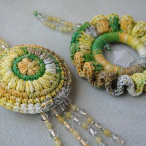 May include: Two crocheted floral earrings made with green, yellow and white yarn. The earrings are attached to a string of beads.