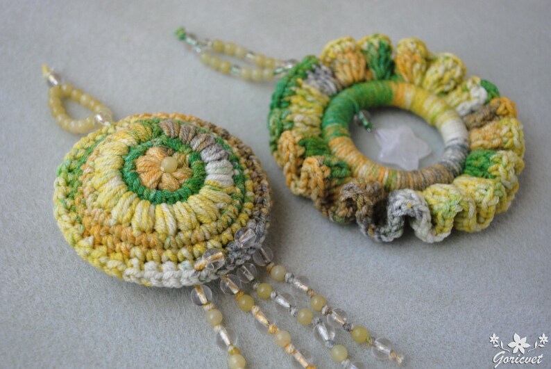 May include: Two crocheted floral earrings made with green, yellow and white yarn. The earrings are attached to a string of beads.