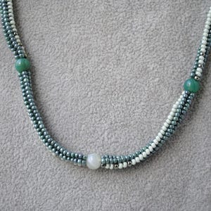May include: A multi-strand necklace with green and white beads. The necklace has a silver-toned metal clasp.