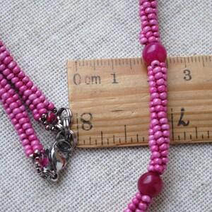 Puede incluir: Un collar de cuentas rosadas con dos cuentas rosadas m&aacute;s grandes y un cierre plateado. El collar se mide con una regla, mostrando que mide aproximadamente 5 cm de largo.