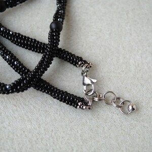May include: A black beaded necklace with a silver clasp and a silver chain. The necklace is made of small black beads and has a silver clasp with a silver chain attached to it.