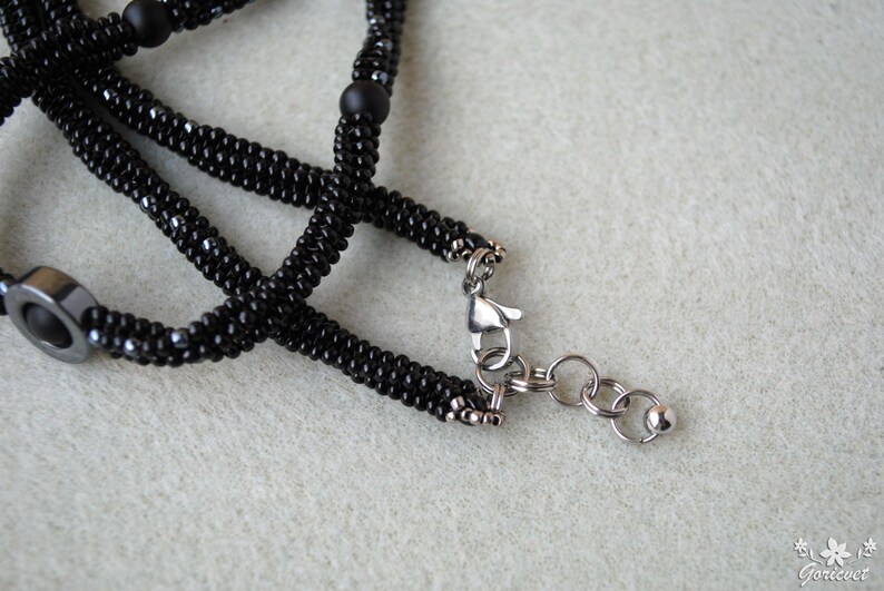 May include: A black beaded necklace with a silver clasp and a silver chain. The necklace is made of small black beads and has a silver clasp with a silver chain attached to it.