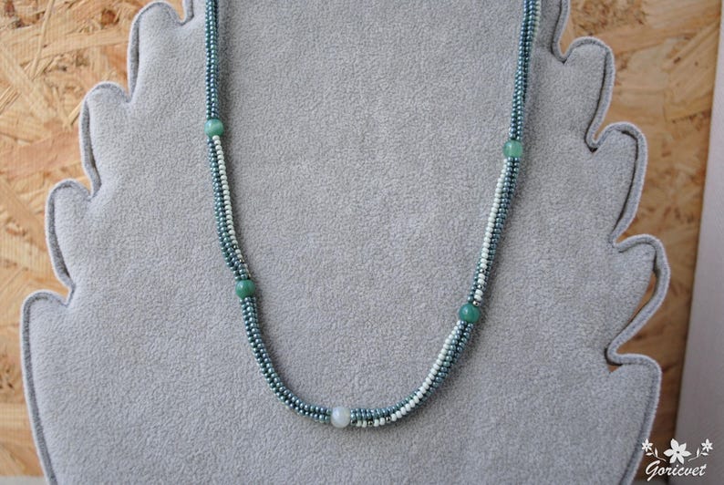 May include: A delicate necklace made with small, light blue and white beads. The necklace has four larger, round, green beads spaced evenly along the length.