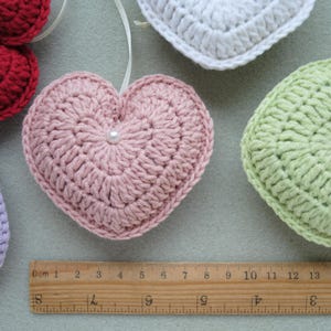 May include: Five crocheted hearts in different colours, including red, pink, green, white, and purple. Each heart has a small pearl button in the centre.