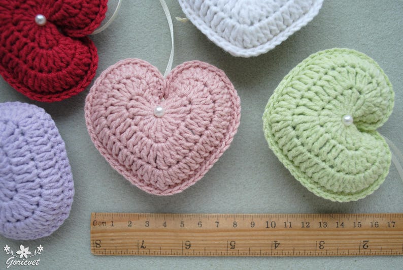 May include: Five crocheted hearts in different colours, including red, pink, green, white, and purple. Each heart has a small pearl button in the centre.