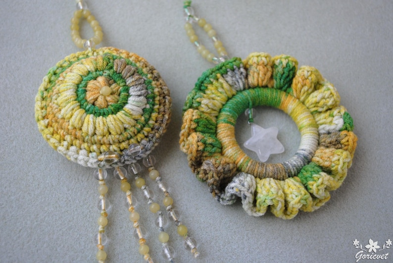 May include: Two crocheted ornaments with a star-shaped charm. One ornament is a circle with a green, yellow, and white pattern. The other ornament is a ring with a green, yellow, and white pattern.