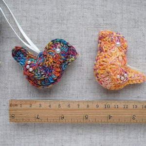 May include: Two crocheted bird ornaments, one with a rainbow pattern and the other with a yellow and orange pattern. Both ornaments have white pearl beads for eyes.