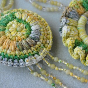 May include: A pair of crocheted flower-shaped pendants in yellow, green and grey. The pendants are attached to a beaded chain.