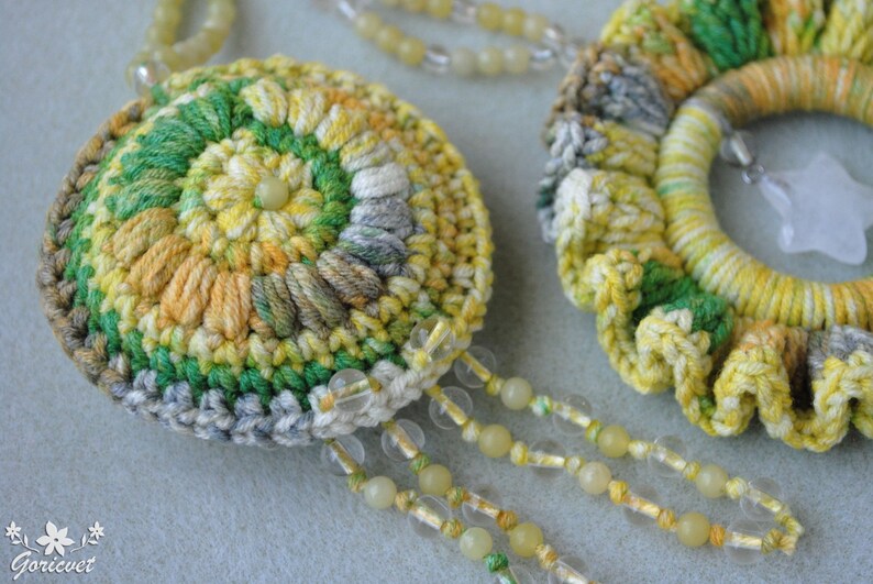 May include: A pair of crocheted flower-shaped pendants in yellow, green and grey. The pendants are attached to a beaded chain.